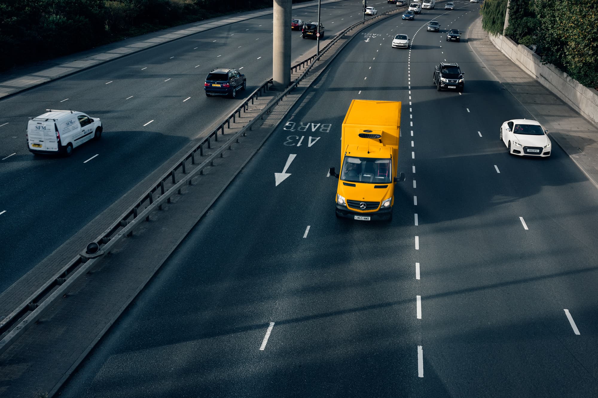 Vista aerea di un'autostrada a più corsie con traffico leggero. Un furgone giallo per le consegne e diverse auto stanno guidando in corsie separate. Un divisore separa il traffico opposto.