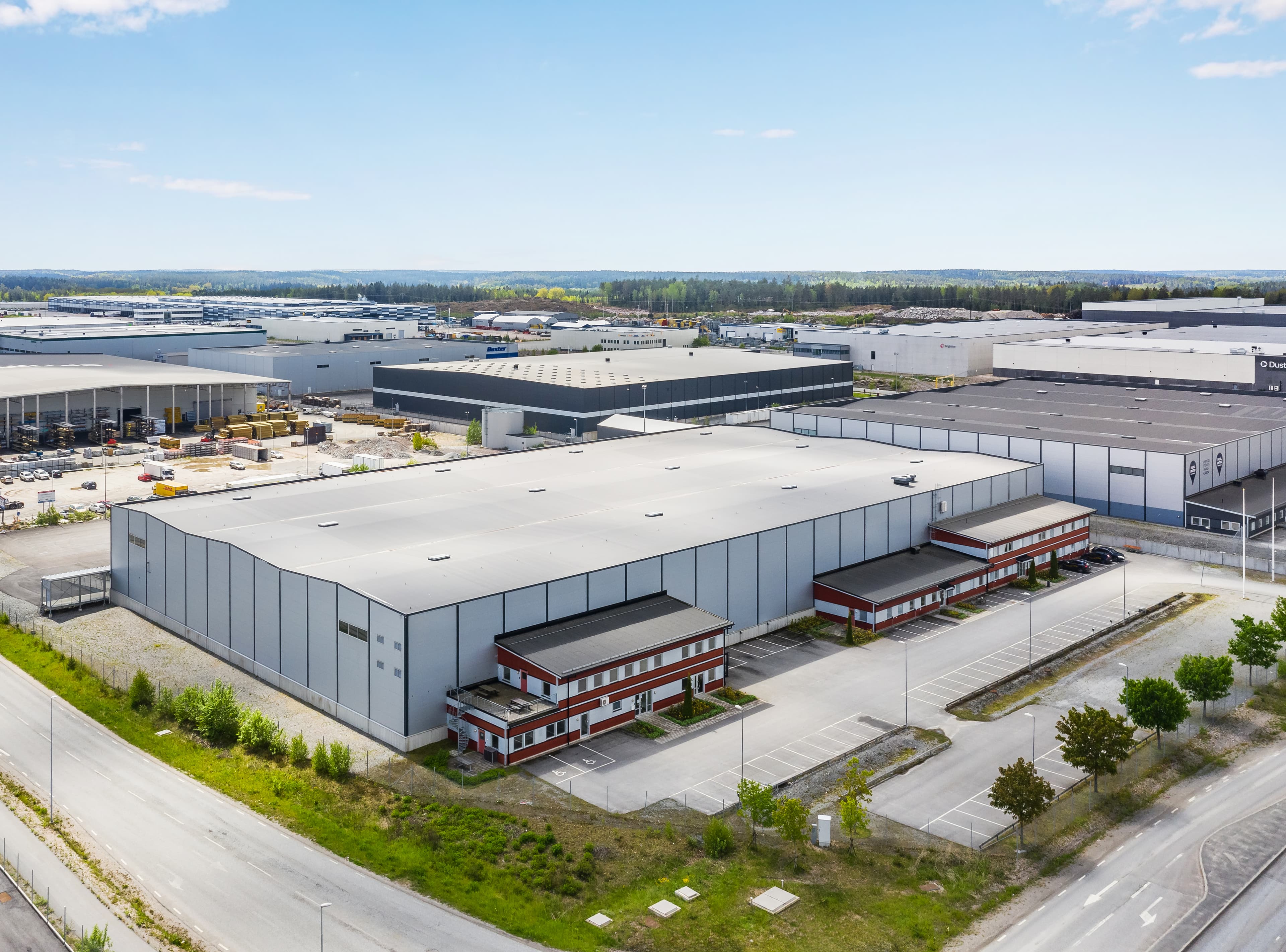 Aerial view of a large industrial warehouse complex with multiple buildings and an adjacent parking lot, surrounded by other similar structures.