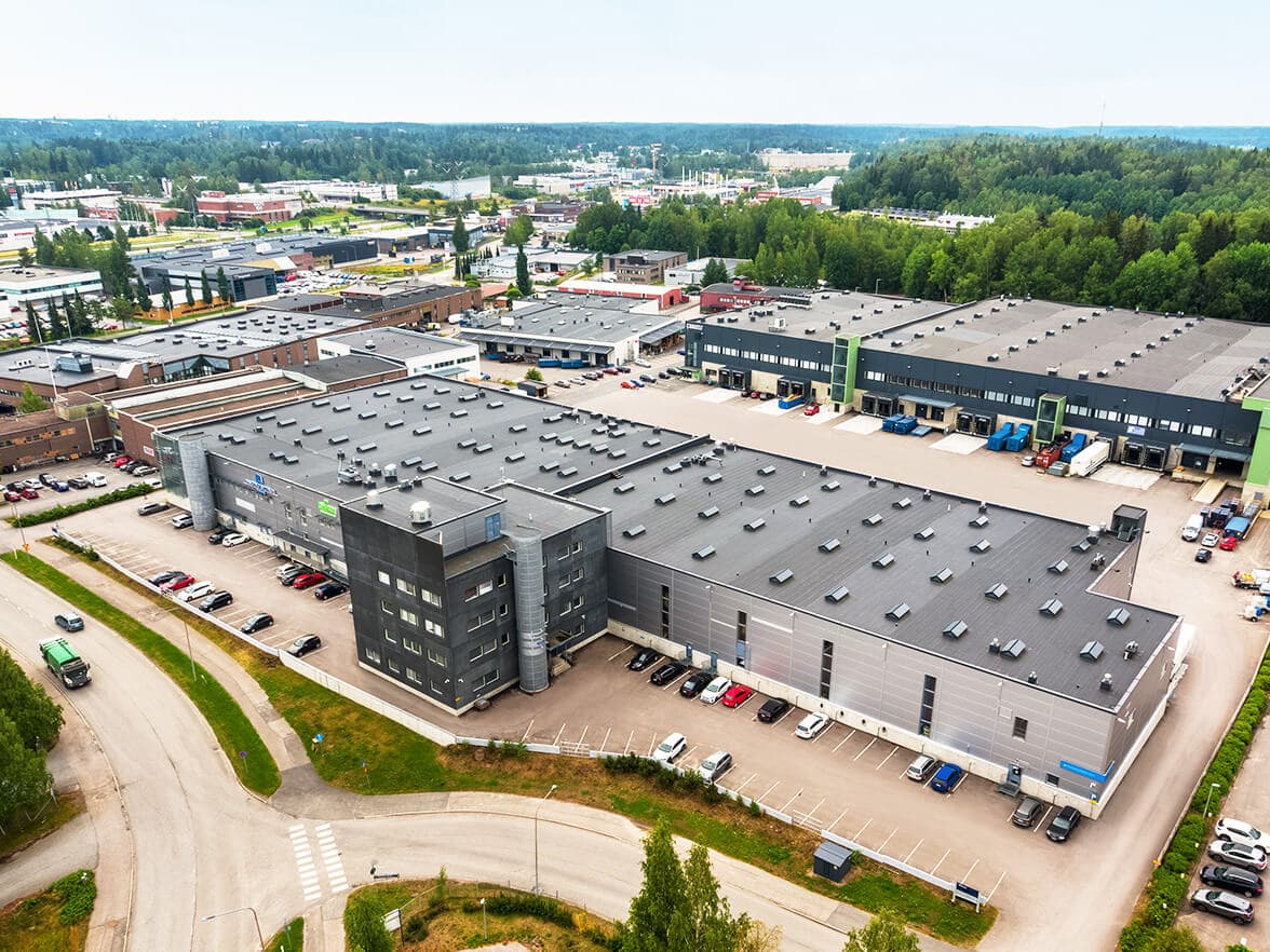 Vista aérea de una gran instalación industrial con múltiples edificios grises, estacionamientos y vegetación circundante.