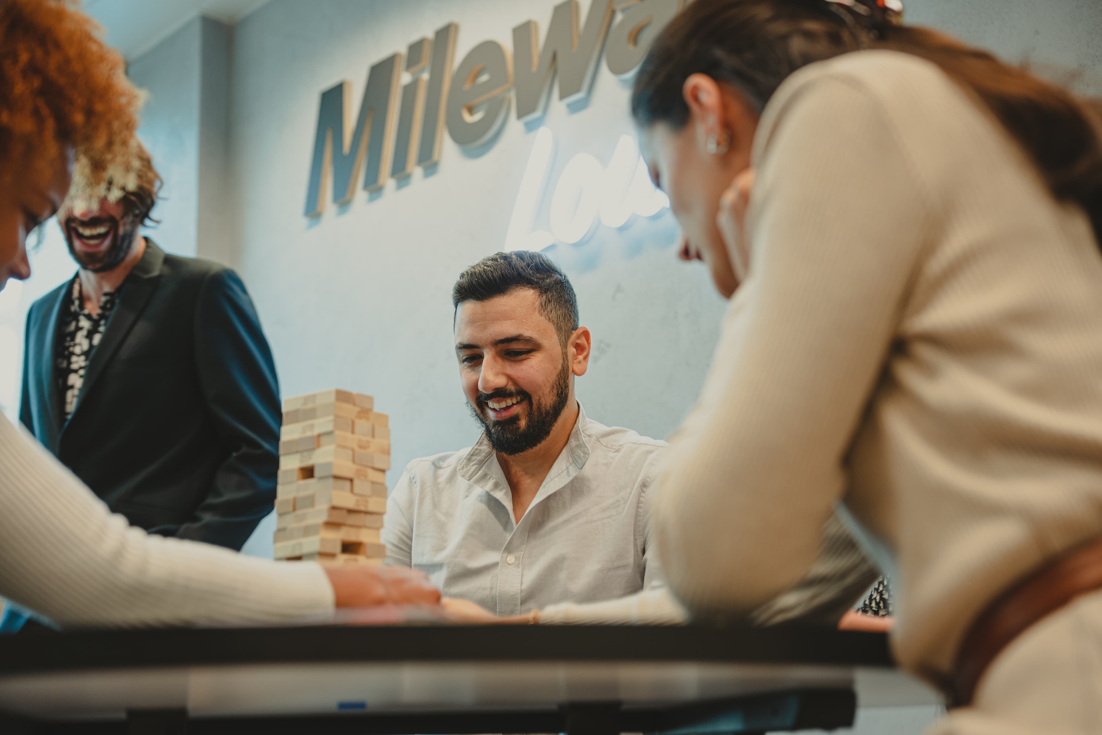 Mensen spelen Jenga aan een tafel met op de achtergrond het logo van Mileway op de muur.