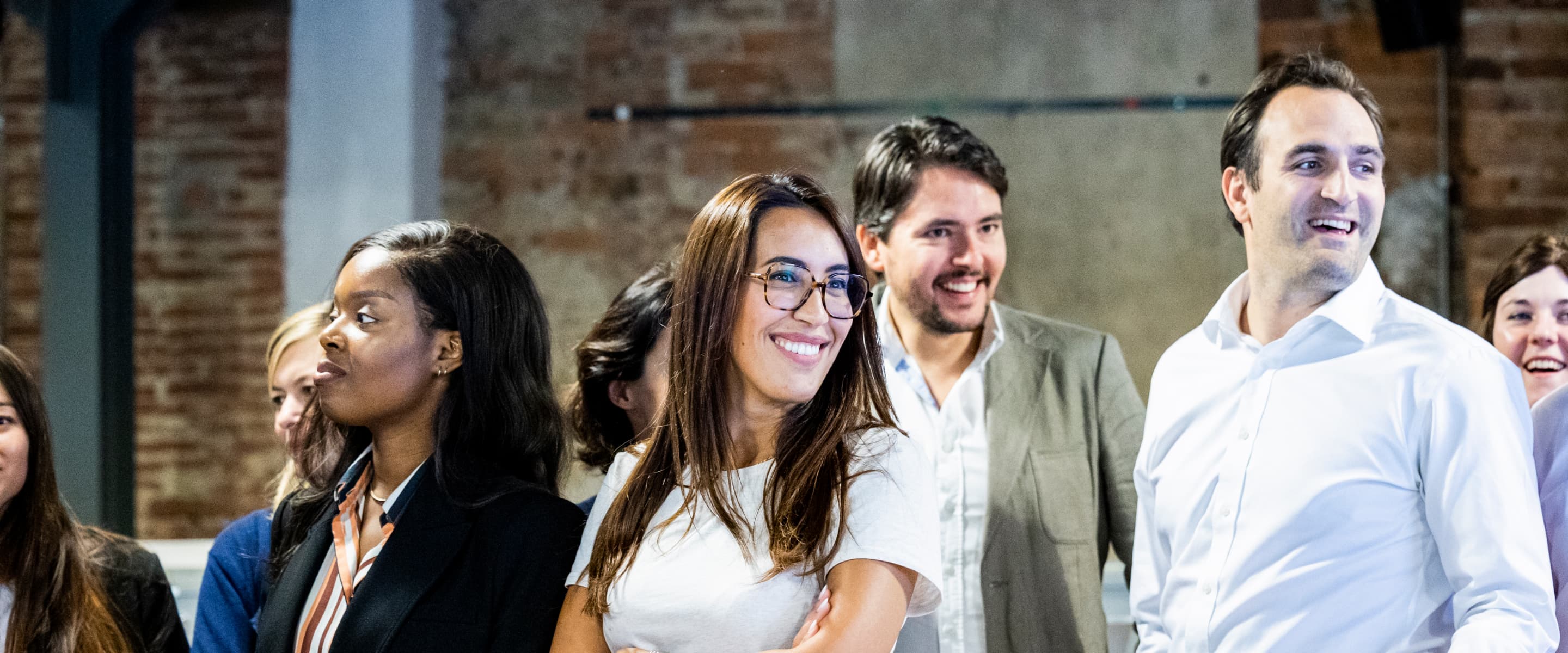 Un groupe de personnes debout ensemble, certaines souriantes, dans un cadre intérieur décontracté.
