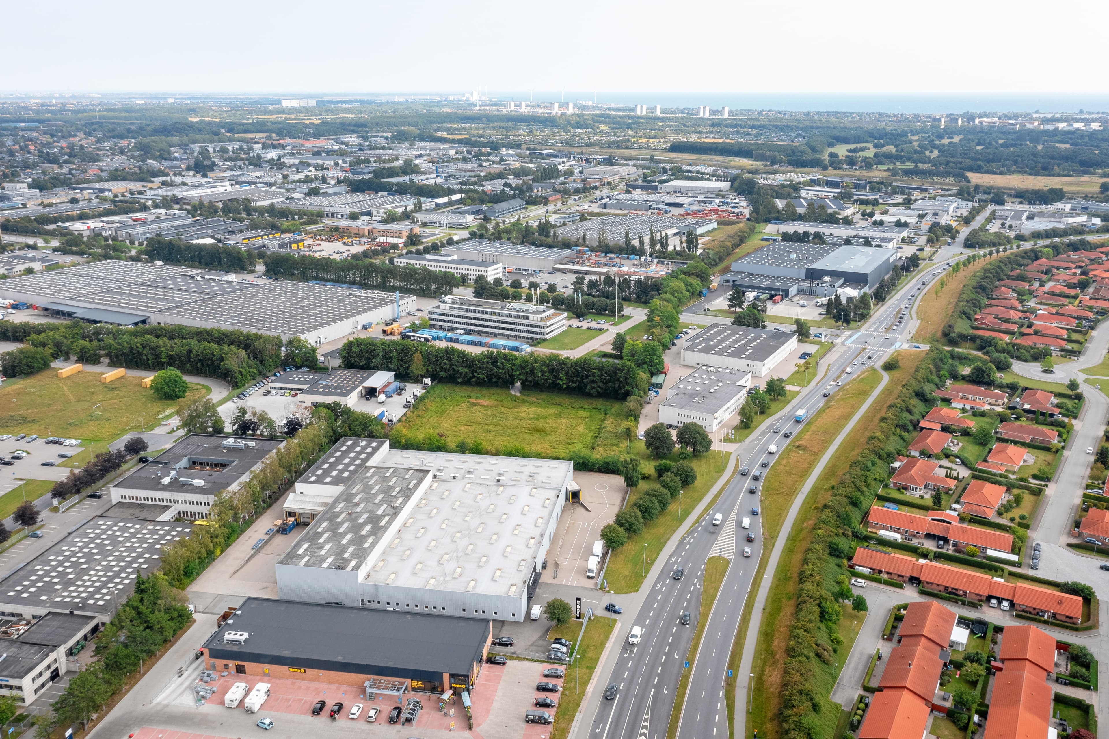 Luftaufnahme eines Industriegebiets mit Lagerhallen, Straßen und Wohnhäusern.