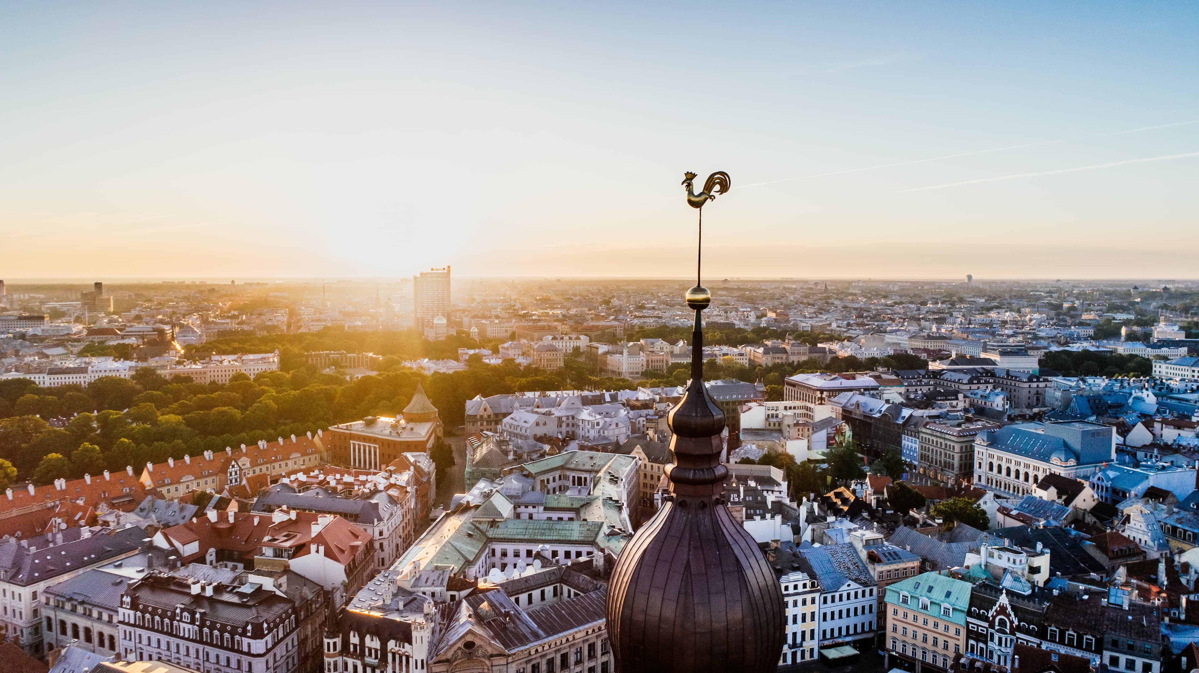 Vista aérea de un paisaje urbano al atardecer, con un destacado campanario de iglesia en primer plano y extensas estructuras urbanas en el fondo.