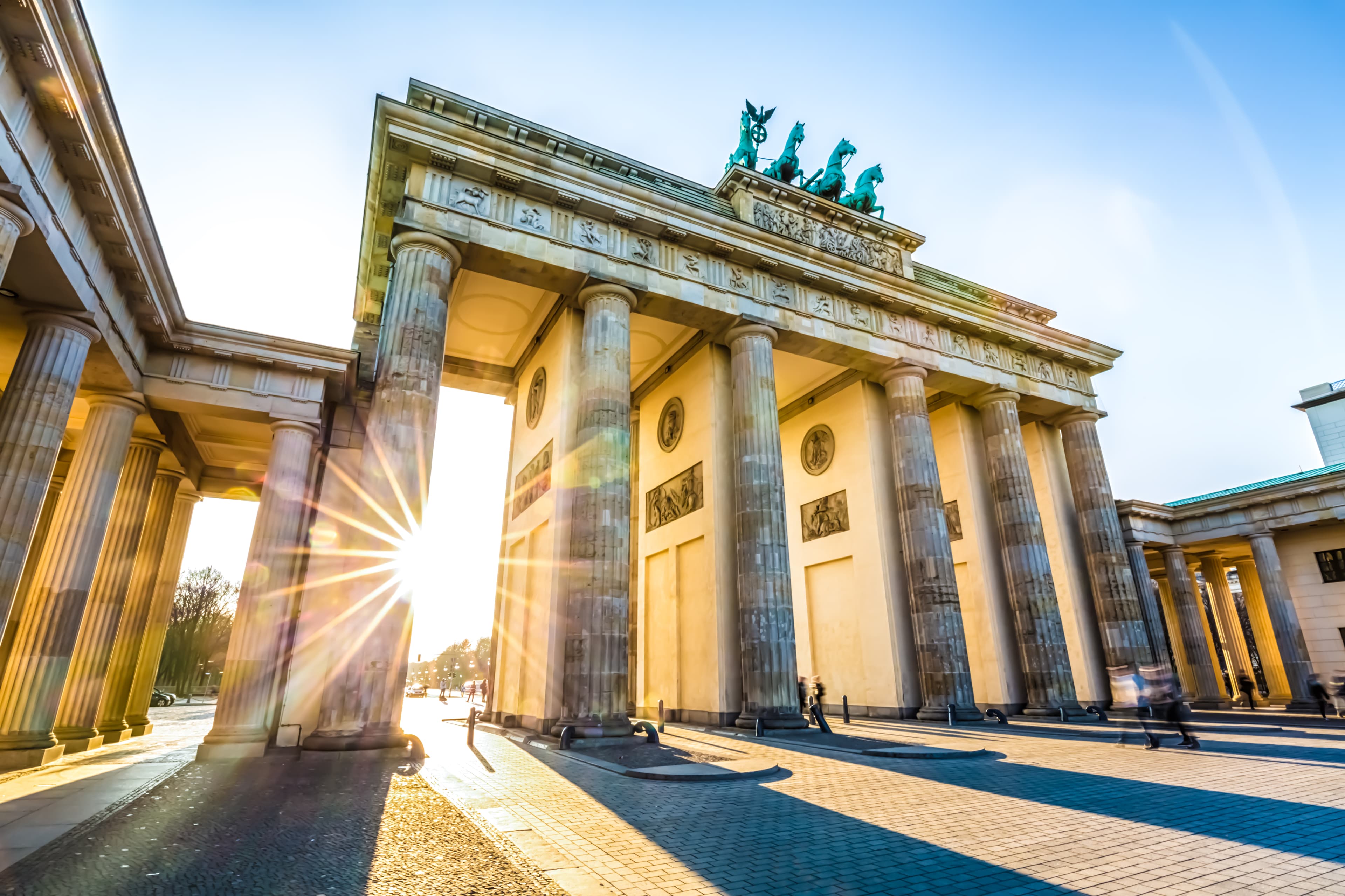 Brandenburger Tor i Berlin, Tyskland, är upplyst av den nedgående solen och kastar långa skuggor på kullerstenstorget.