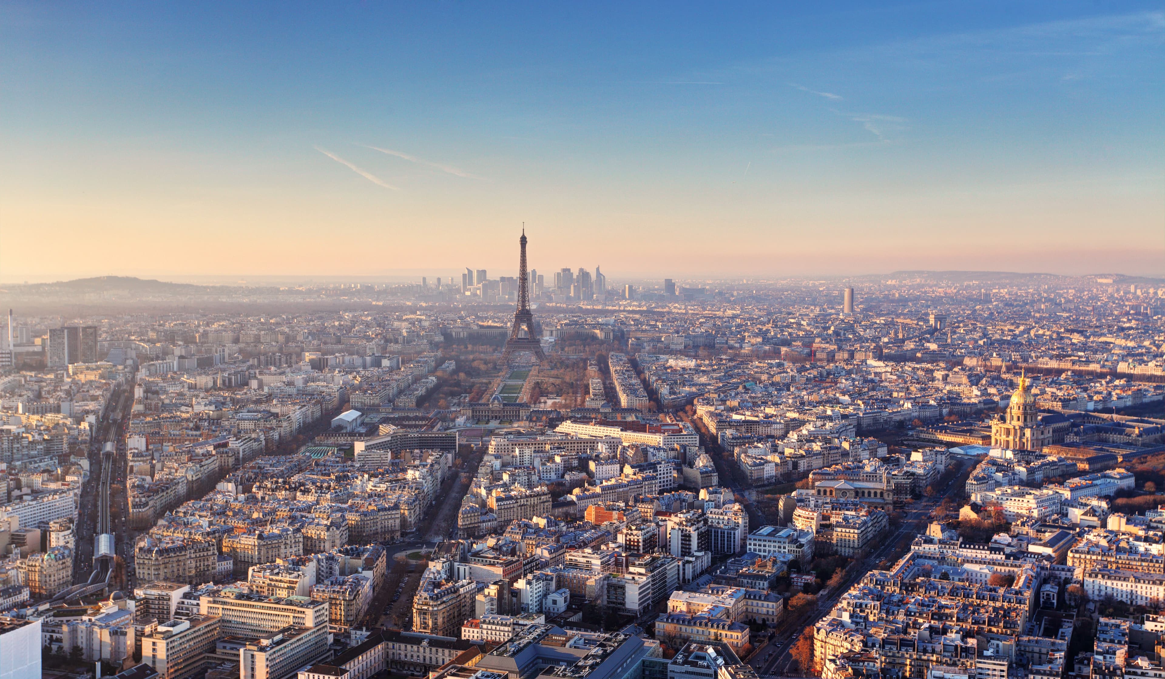 Flygfoto över Paris vid solnedgången, med Eiffeltornet och stadsbilden med byggnader utspridda över horisonten under en klar himmel.