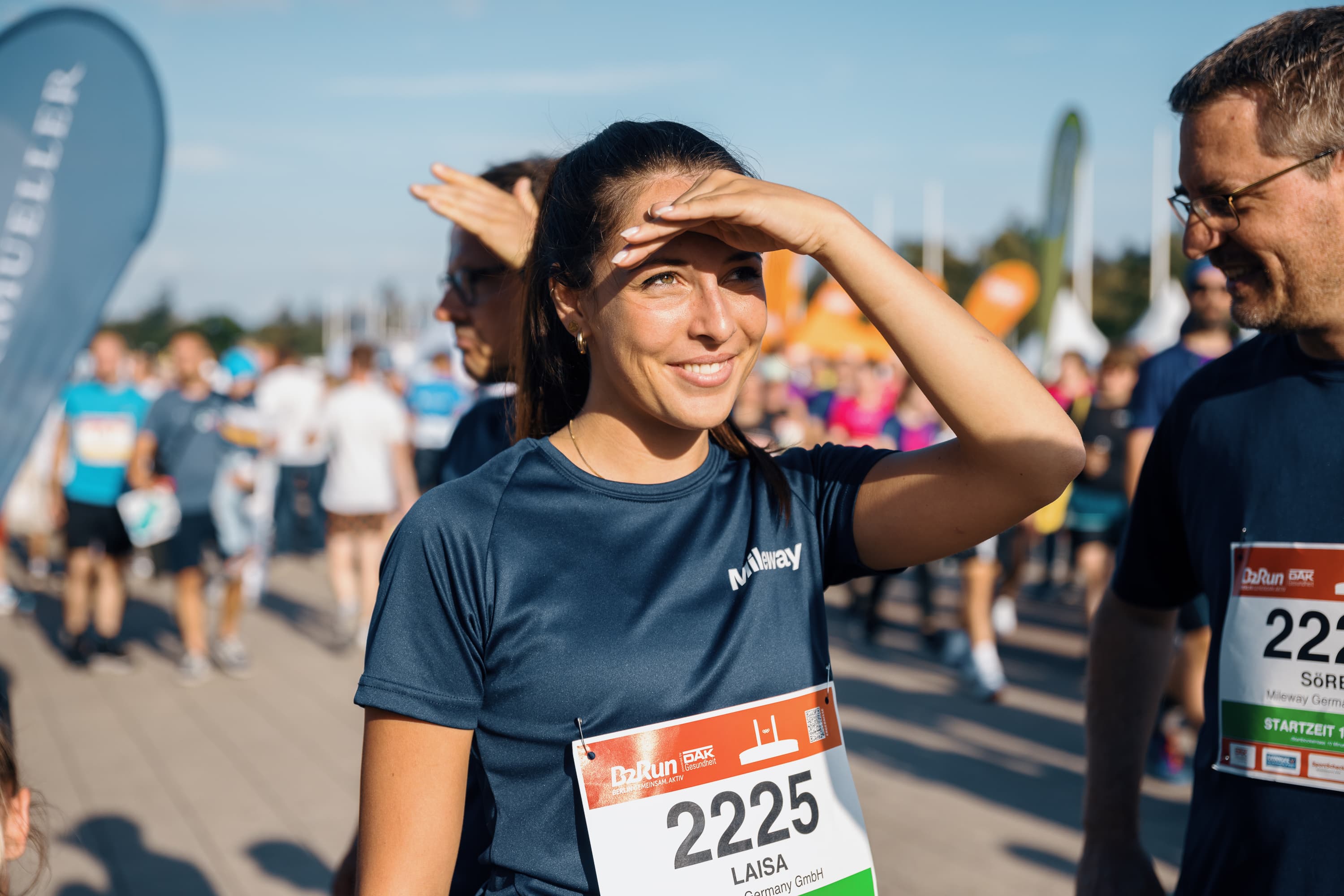 Een vrouw met startnummer 2225 schermt haar ogen af tegen de zon te midden van een groep hardlopers.