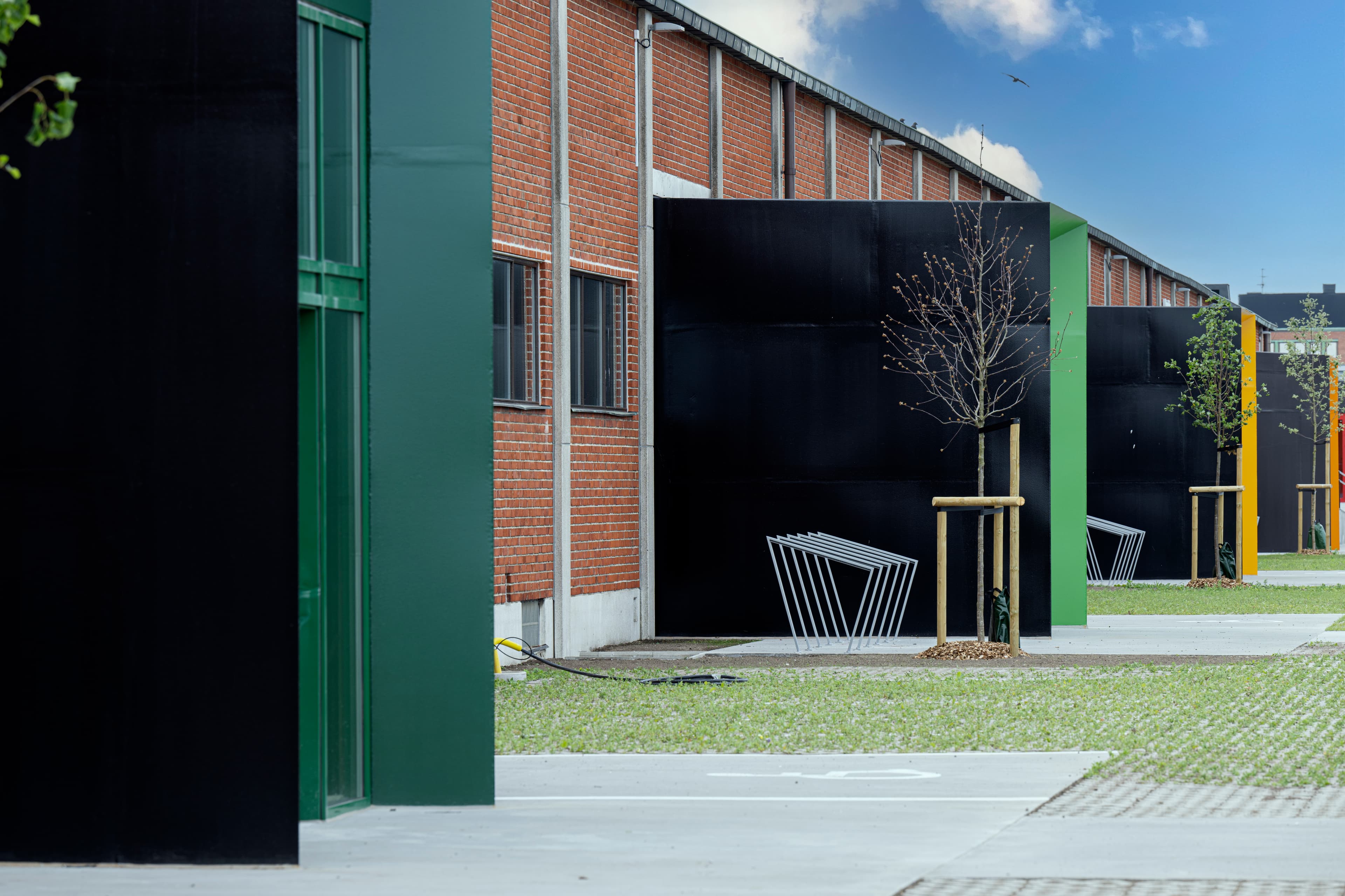 Industriel bygning med mursten og sort metalfacade med små træer og metalbænke langs en gangsti.