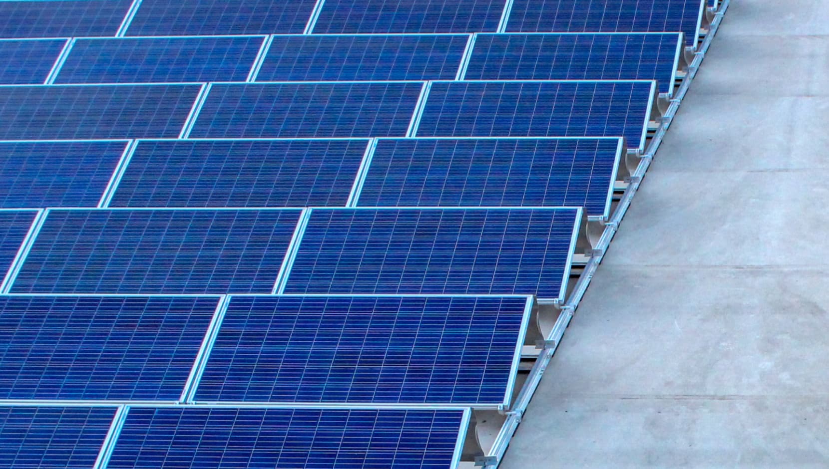 Reihen blauer Solarmodule, die auf einer Betonoberfläche installiert sind.