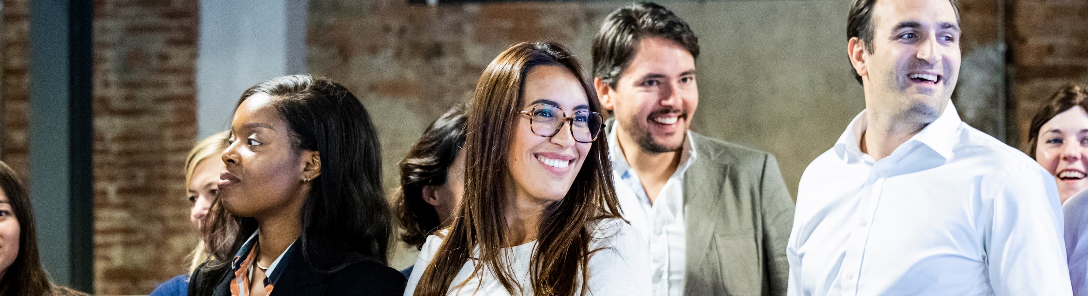 Un gruppo di persone sorridenti che guardano in direzioni diverse, in piedi in un ambiente informale.