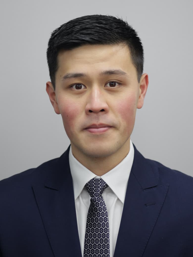 A person in a suit and tie is posing against a plain gray background.