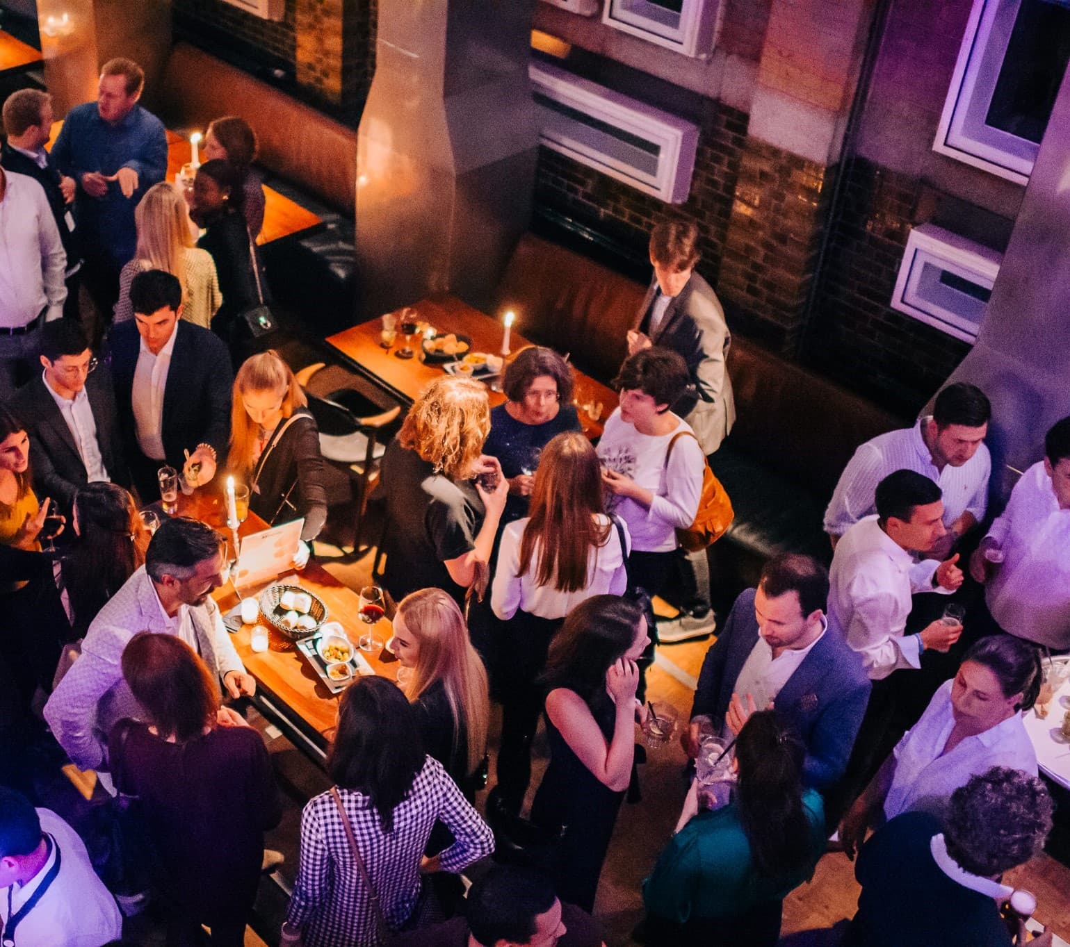 Een grote groep mensen komt bijeen op een levendig binnenevenement met gedempt licht en kaarsen op tafels.