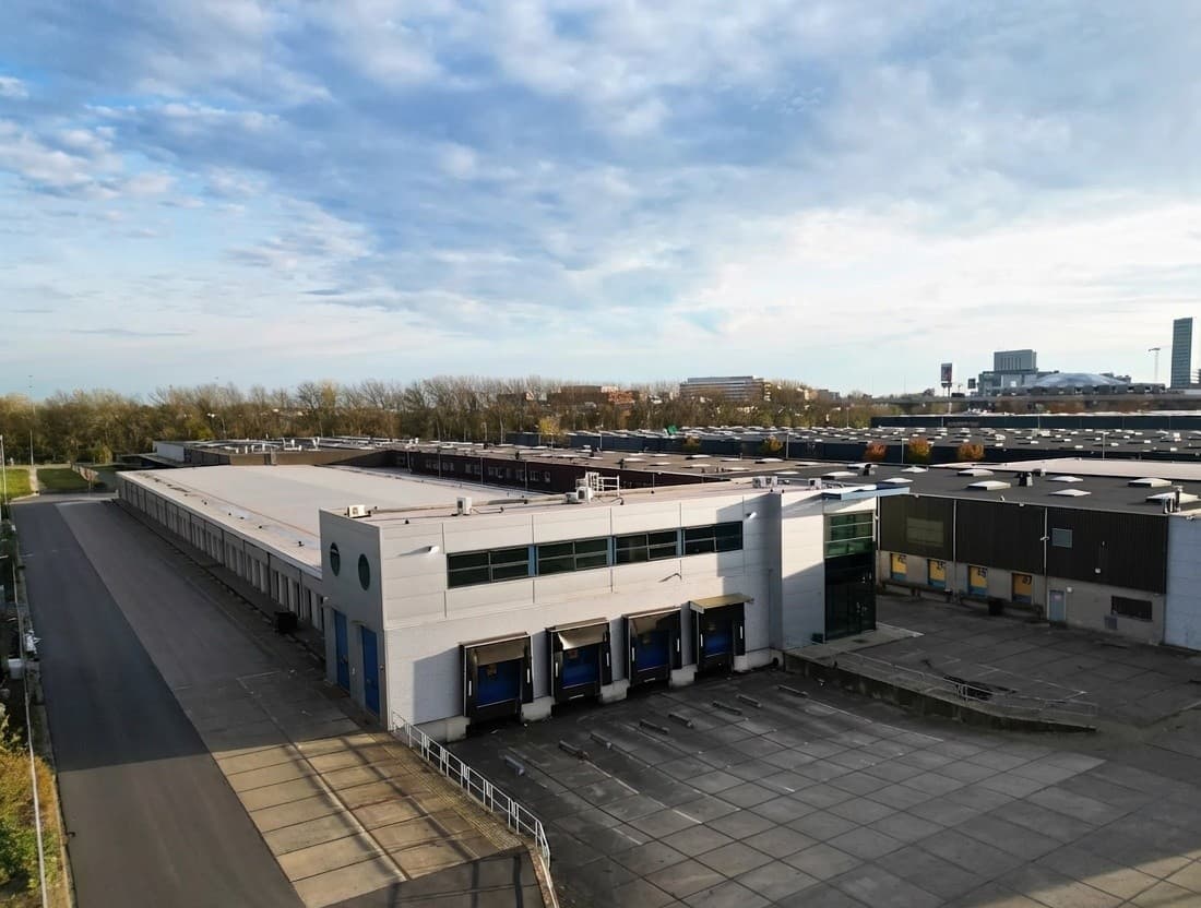 A large, modern warehouse with several loading bays and an empty car park nearby beneath a partly cloudy sky.