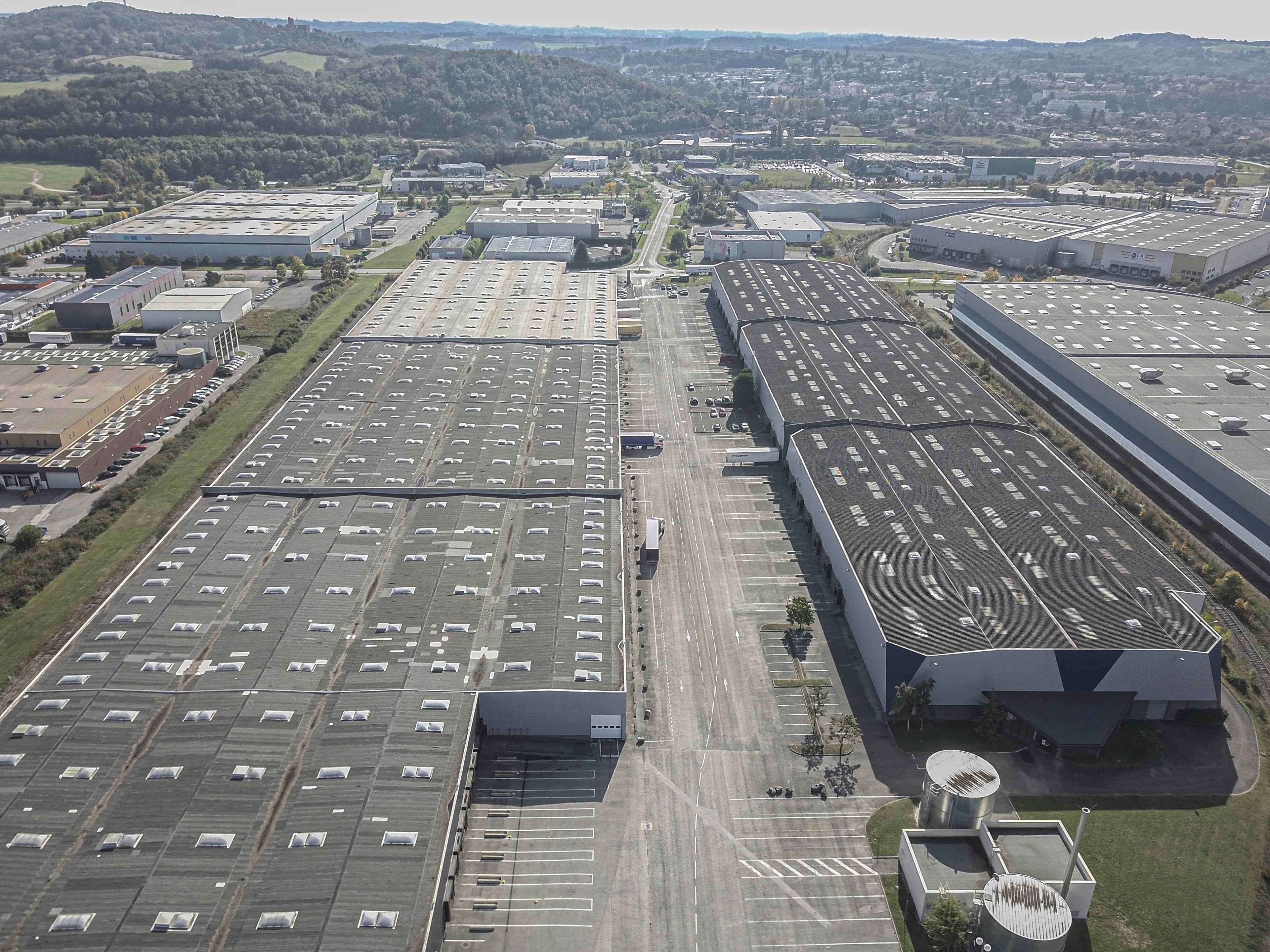 Aerial view of a large industrial complex featuring warehouses, car parks, and green areas surrounding the site.