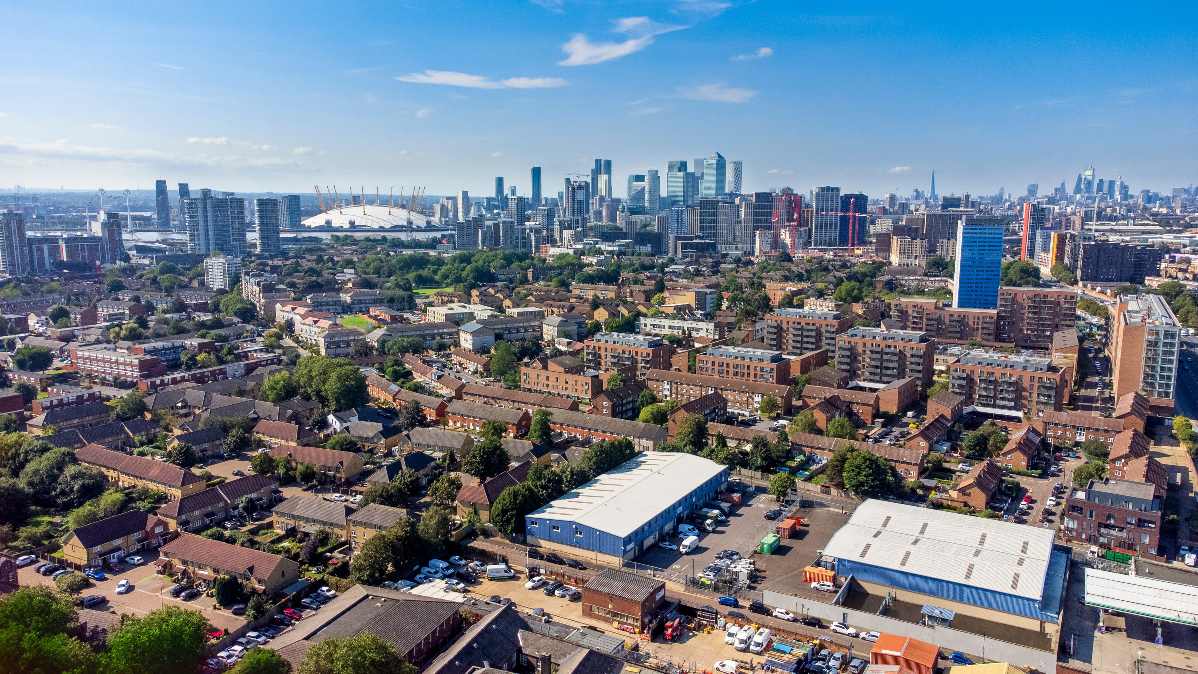 Aerial view of a residential urban area with mid- and high-rise buildings in the background beneath a clear blue sky.