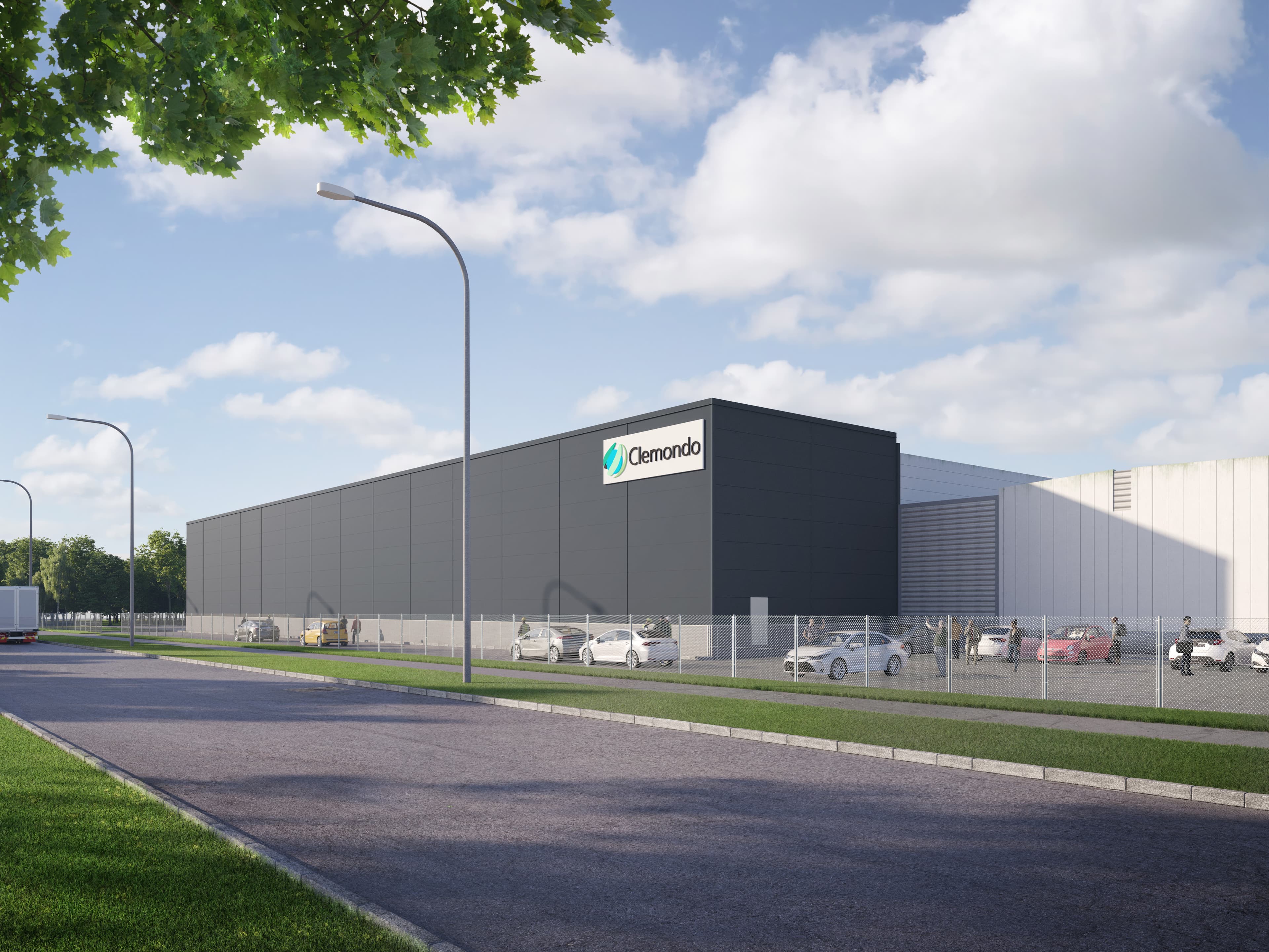 A modern industrial building with an Olamondo sign, fenced and bordered by parked cars, beneath a partly cloudy sky.