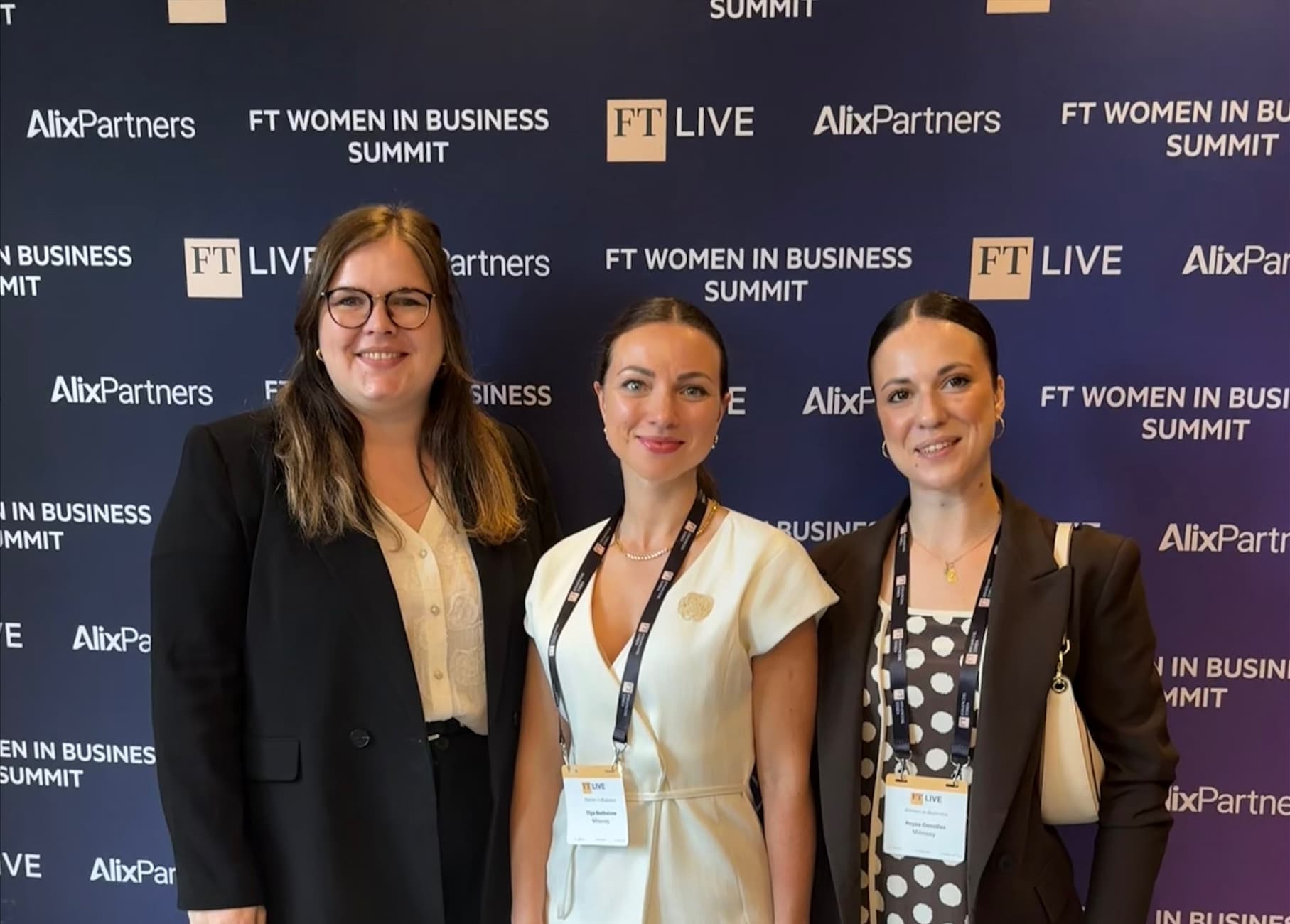Three people stand together posing for a photo at the FT Women in Business Summit, wearing business attire with event badges.