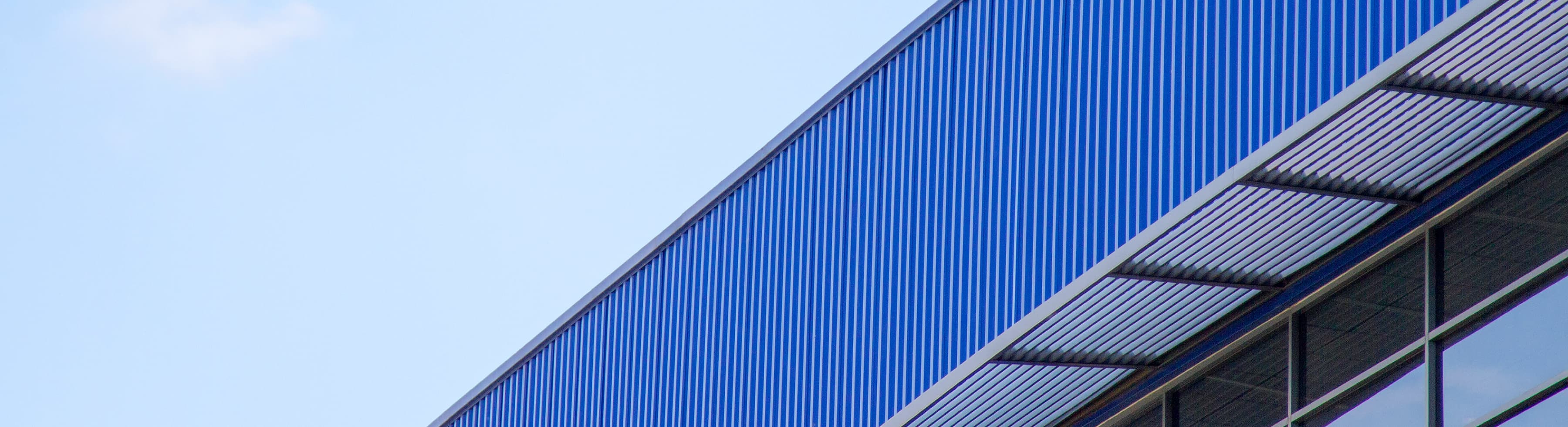 A close-up of a modern building's exterior with blue corrugated metal panels and a row of windows under a clear sky.