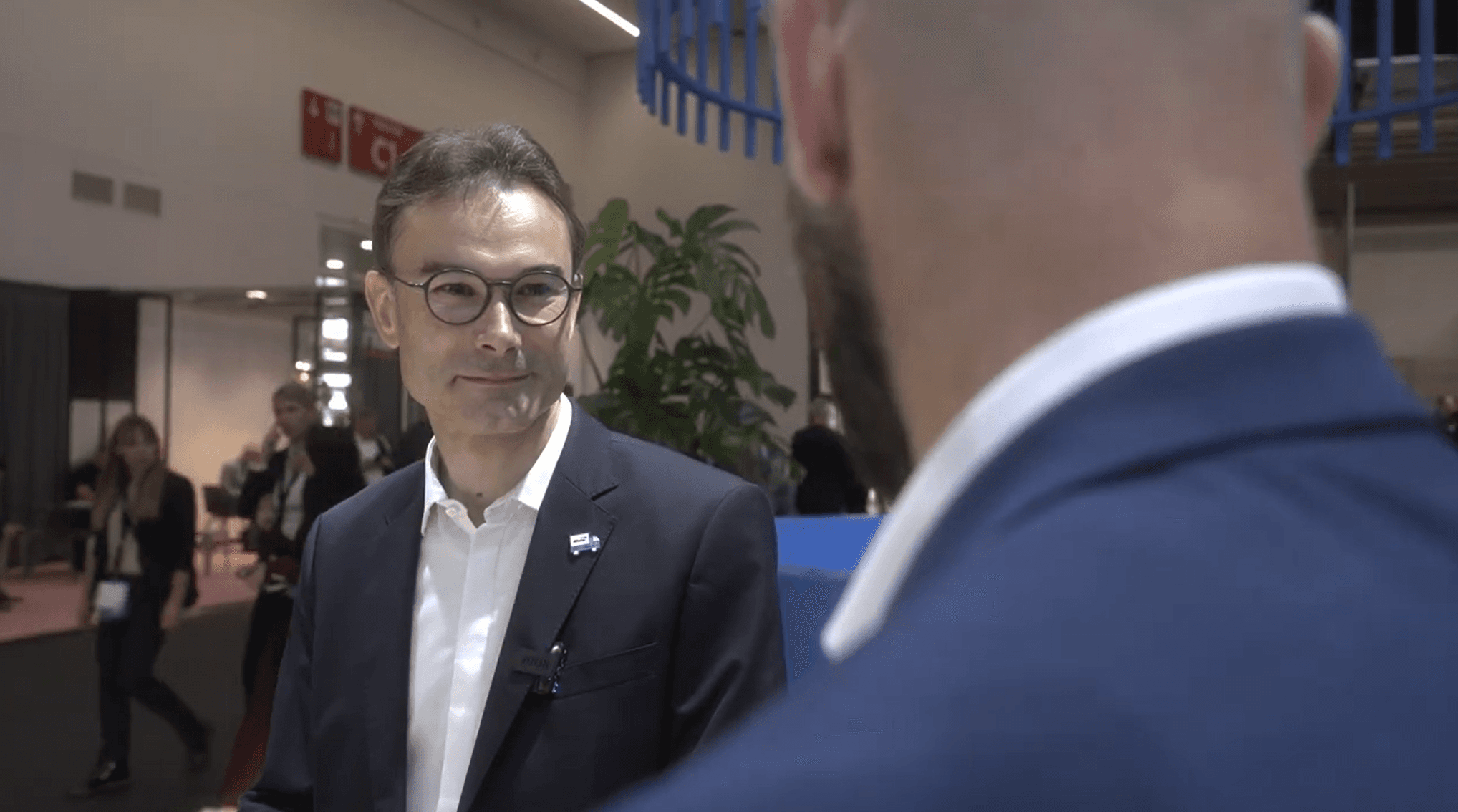 Two people in suits conversing at an indoor event.
