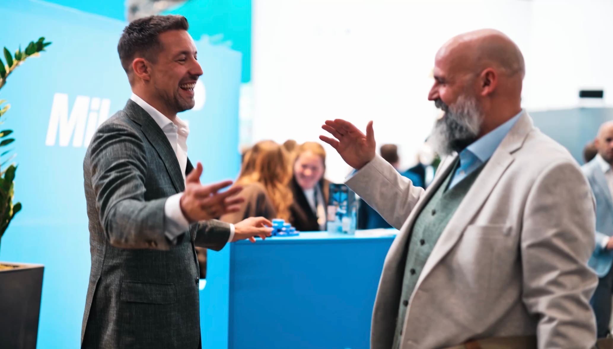 Two individuals in business attire greeting each other with gestures in a conference setting.
