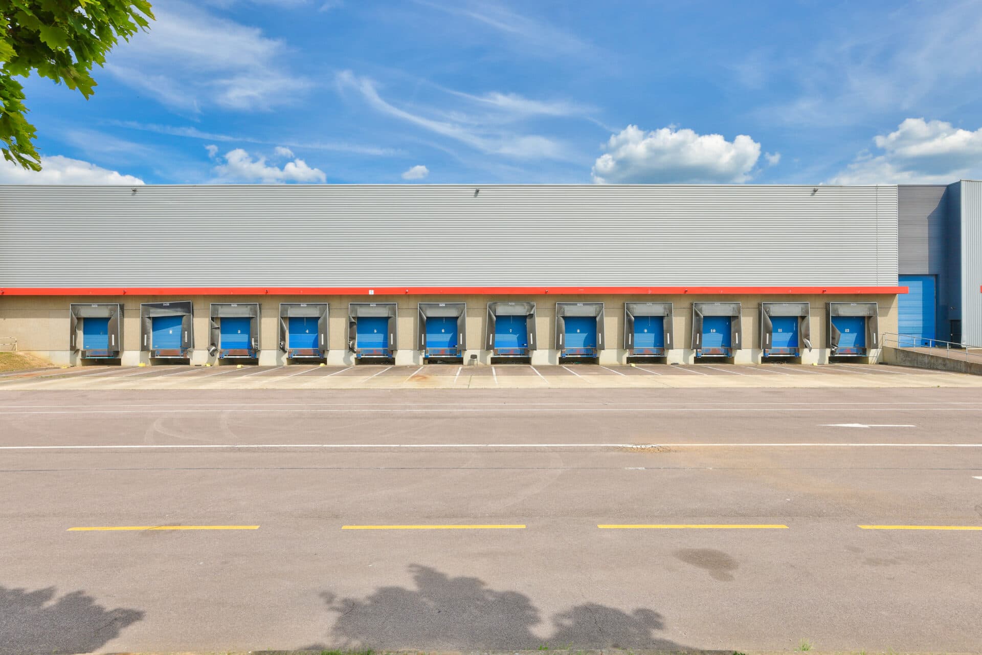 A warehouse exterior with a row of ten blue loading bay doors and an empty tarmac lot.
