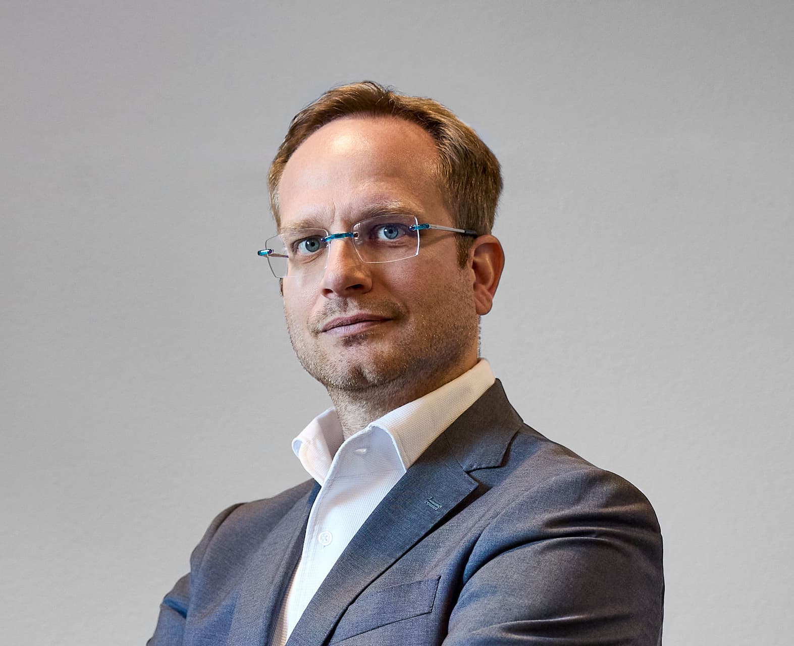 A person in a suit and glasses stands with their arms folded.